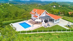 Una casa moderna con piscina, un patio con poltrone relax e vista sulle colline circostanti.