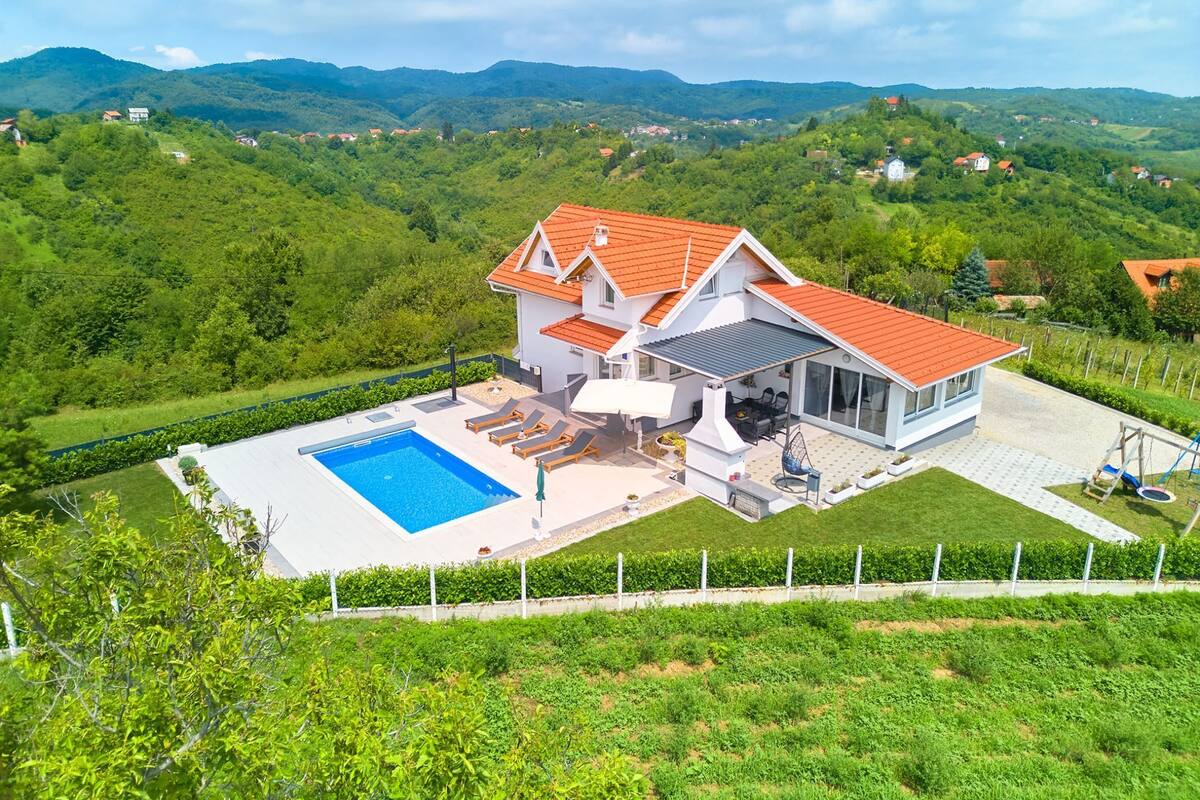 Ein modernes Haus mit Swimmingpool, einer Terrasse mit Liegestühlen und Blick auf die umliegenden Hügel.
