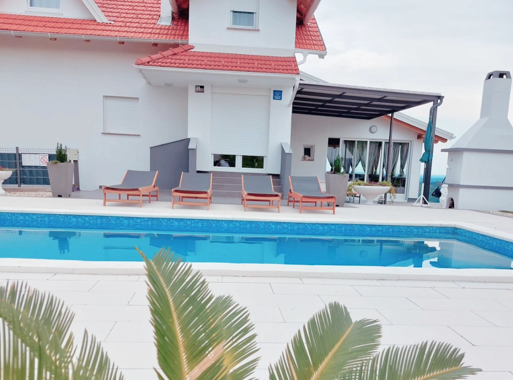 A modern building with a swimming pool, red-tiled roof, and outdoor seating area.