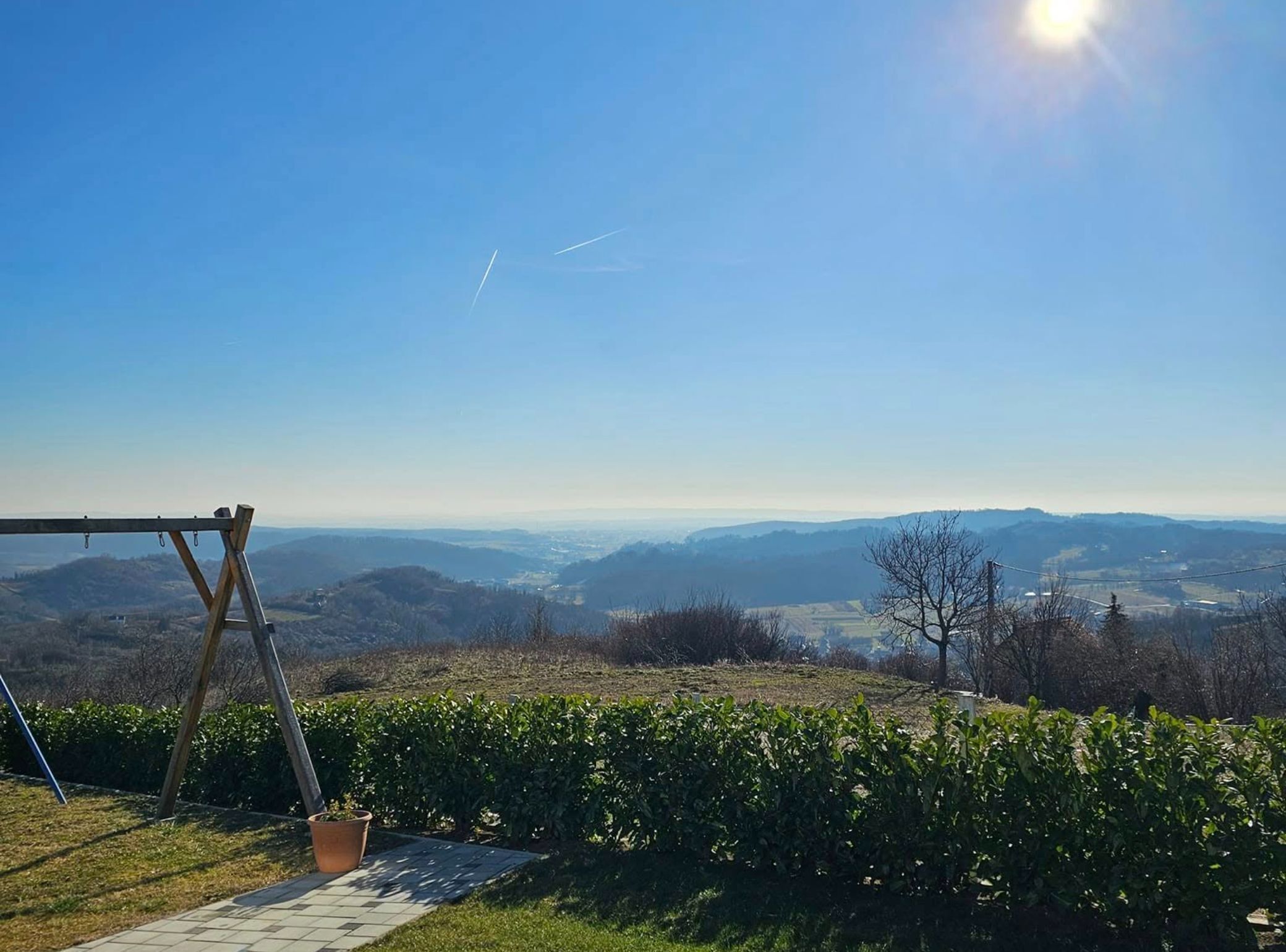 A patio with a swing set overlooking a valley with distant mountains and a clear sky.