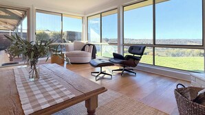 A spacious room with large windows, a wooden table, a white armchair, and a black office chair. - Wineries, Rolling Hills, Alpacas and Chickens (Clarendon)