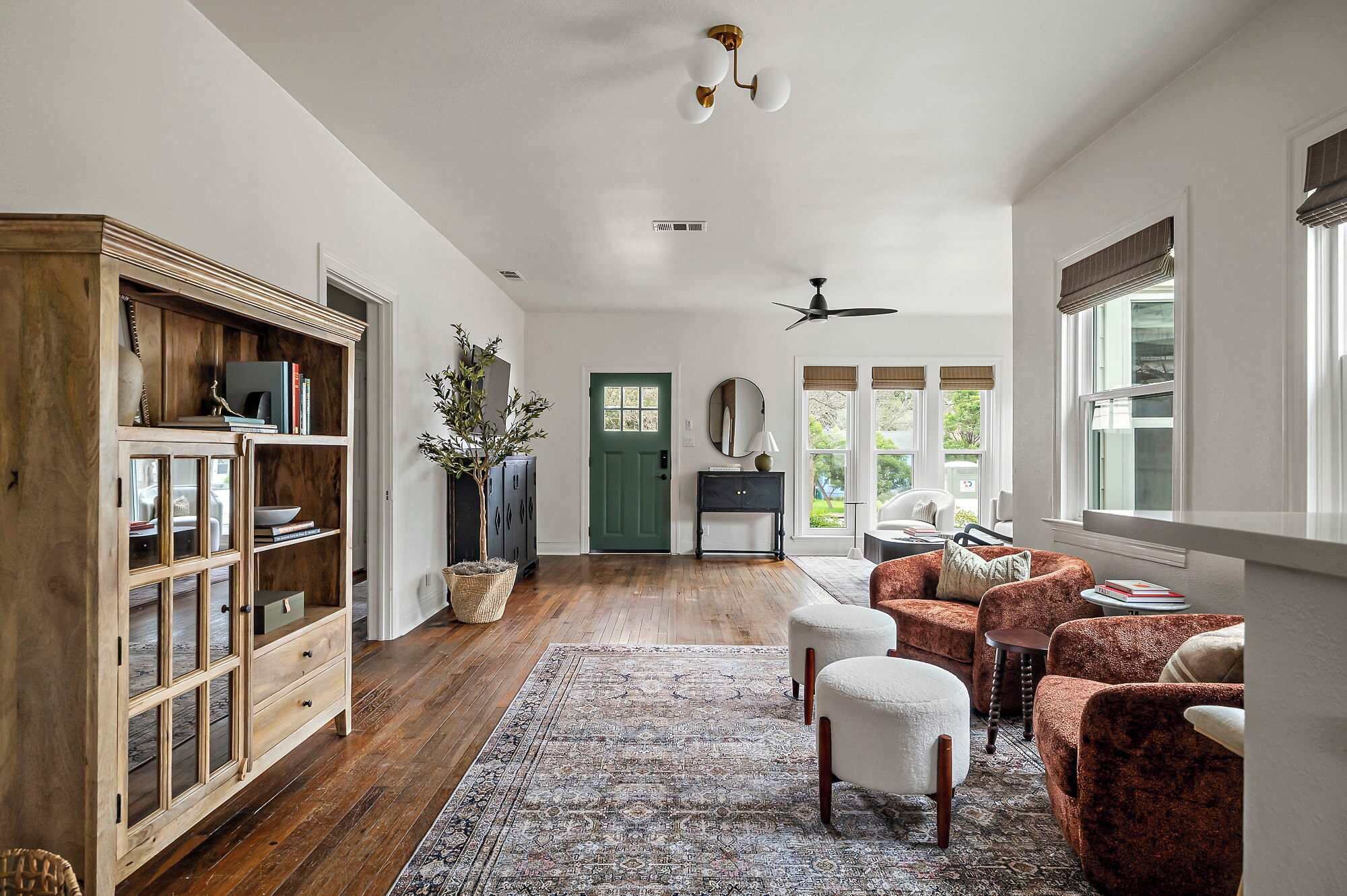 A spacious room with a wooden cabinet, a green door, a round mirror, and a ceiling fan.