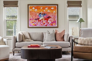 Een woonkamer met een bank, een bijzettafeltje en een schilderij aan de muur.