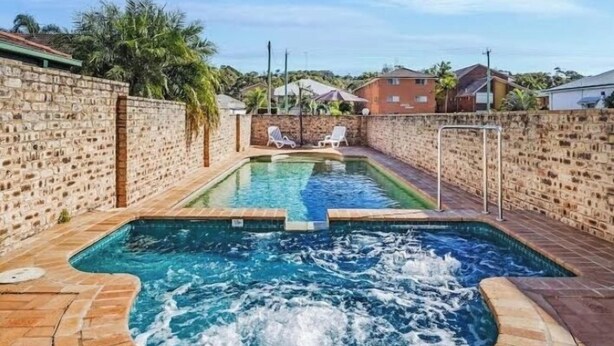 Une piscine avec un jacuzzi au centre, entourée de murs en briques et sous un ciel dégagé.