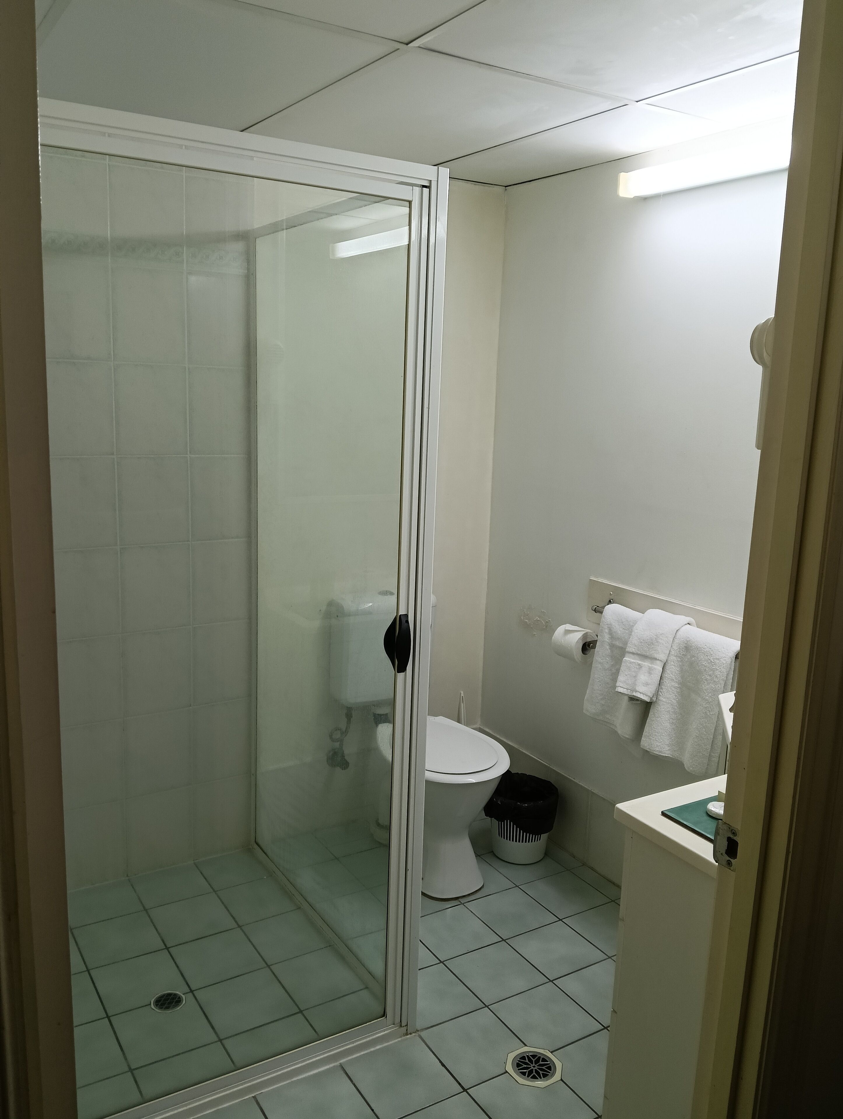 Un baño pequeño y limpio con cabina de ducha de vidrio, inodoro y lavamanos con espejo.
