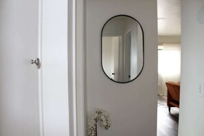 A hallway with a white door, a round mirror on the wall, and a small white flower arrangement.