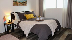 A neatly arranged bedroom with a bed, bedside table, lamp, and a painting on the wall.