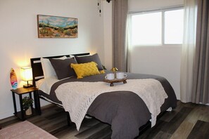 Un dormitorio ordenado con cama, mesita de noche, lámpara y un cuadro en la pared.