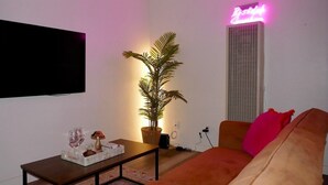 A living room with a sofa, a coffee table, a potted plant, and a neon sign.