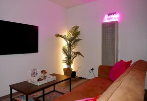 Ein Wohnzimmer mit einer Couch, einem Couchtisch, einer Topfpflanze und einem Neonlichtschild.