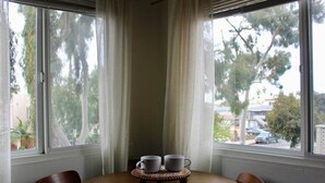 A corner room with a table and two chairs, a window with curtains, and a view of trees and buildings outside.