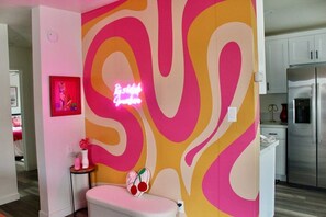 Eine moderne Küche mit Edelstahlgeräten, einer pinkfarbenen Akzentwand und einer Neonreklame.