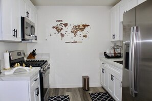 A modern kitchen with white cabinets, stainless steel appliances, and a world map on the wall.