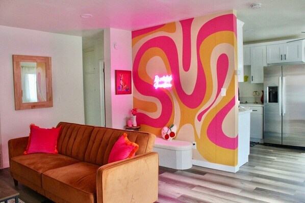Ein modernes Wohnzimmer mit einer Couch, einem kleinen Tisch und einer farbenfrohen abstrakten Wand.