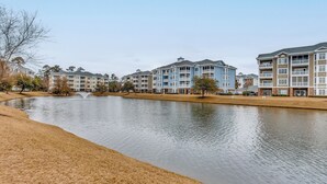 Vue sur un quartier résidentiel donnant sur un lac, avec des immeubles à plusieurs étages, une plage de sable et une fontaine.