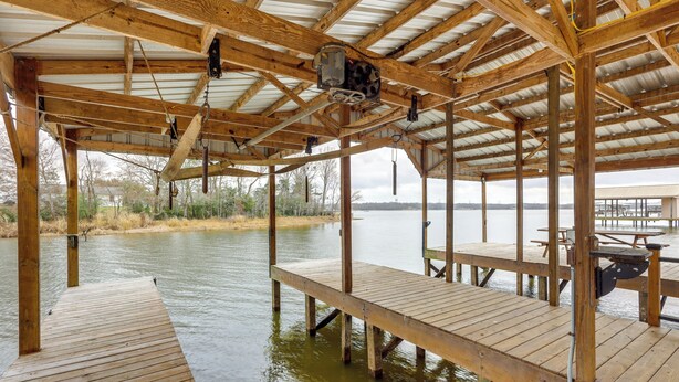 Une structure de terrasse en bois, construite au-dessus de l’eau, avec des bancs et des tables, soutenue par des poutres en bois et surmontée d’un toit en métal.