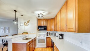 Une cuisine moderne avec des meubles en bois, un plan de travail blanc, des appareils en acier inoxydable et des luminaires suspendus.