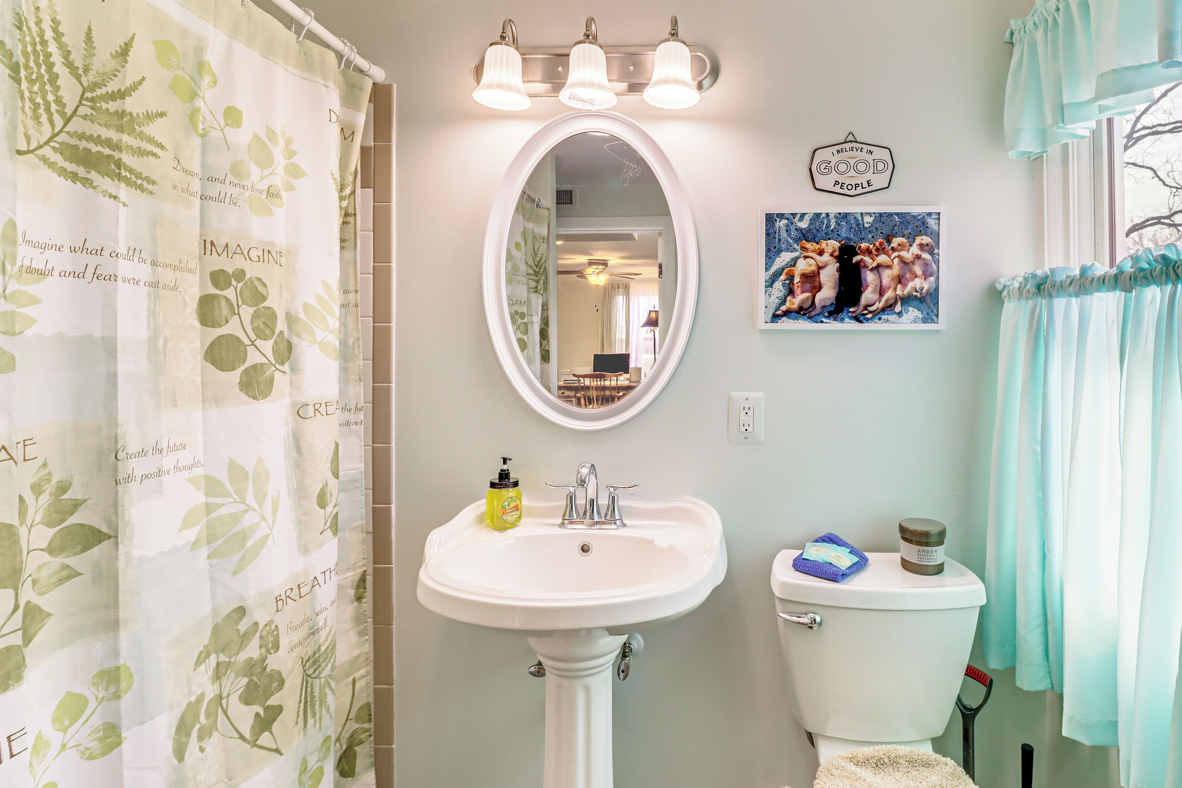 Une salle de bain avec un lavabo blanc, un miroir, des toilettes et un rideau de douche orné d’un motif de feuilles.