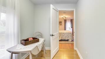 Una habitación con una mesa, una silla, una cama con colcha estampada y una puerta que da a otra estancia.