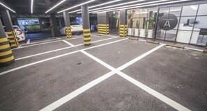 A parking garage with marked parking spaces, yellow and black striped bollards, and a white car parked inside. - Hotel A (Seoul)