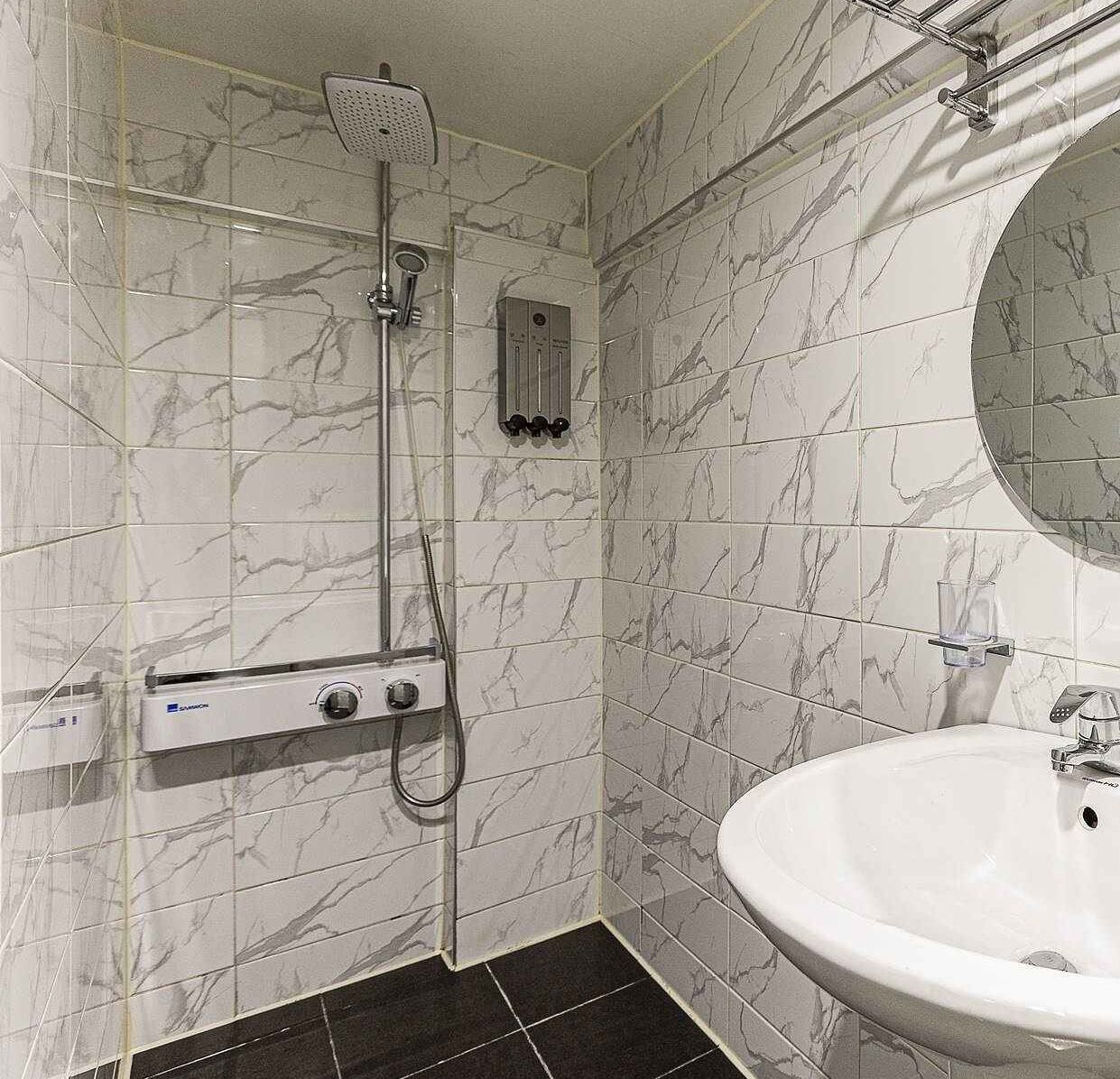 A bathroom with a white sink, a mirror, a shower with a handheld showerhead, and a control panel.