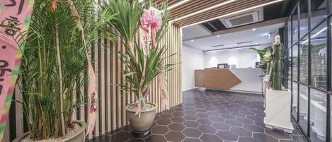 Un hall d’hôtel moderne avec un comptoir d’accueil, des plantes en pot et un sol carrelé à motifs hexagonaux.