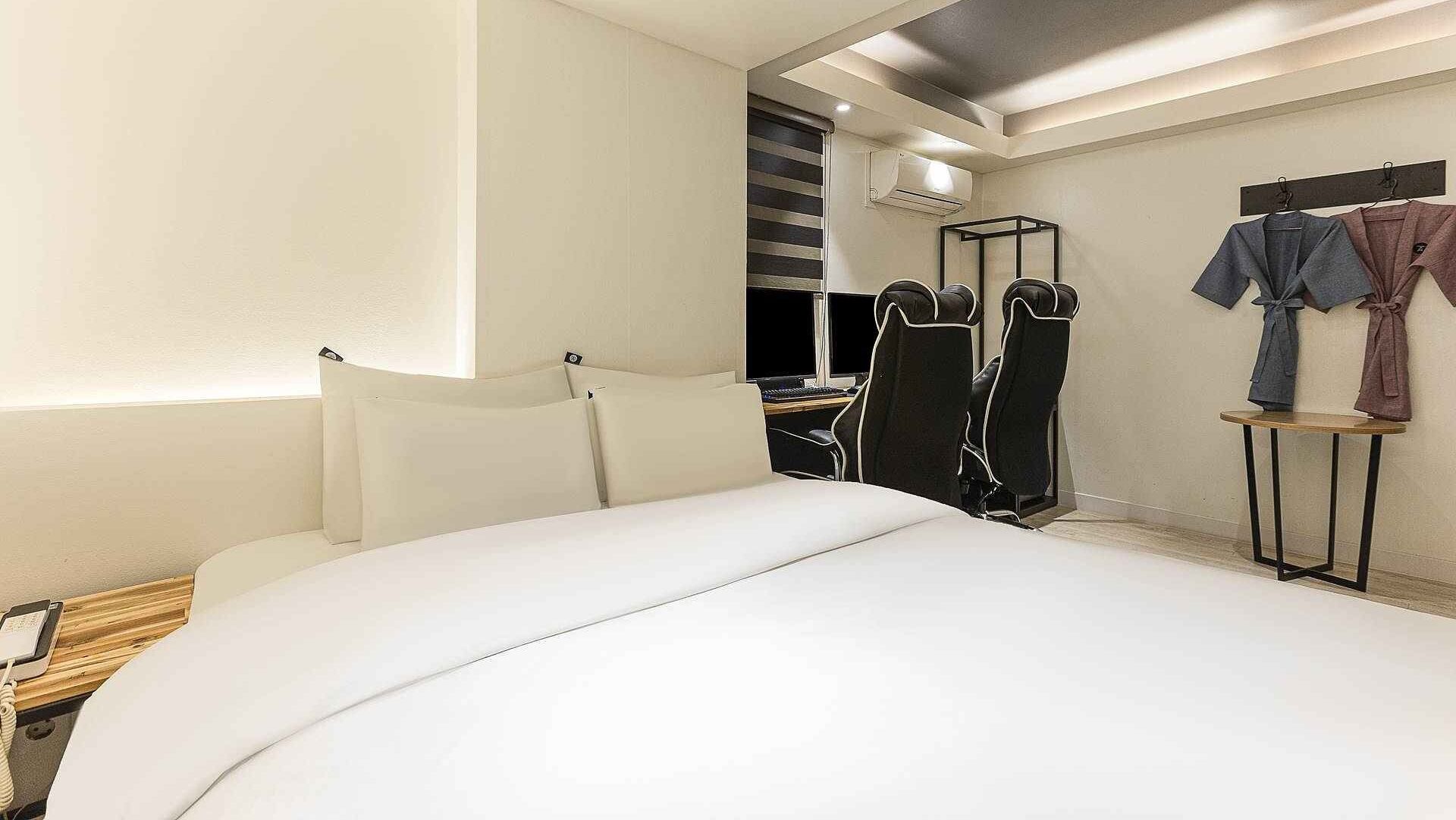 A hotel room with a large bed, a desk with a computer, and a seating area with chairs.