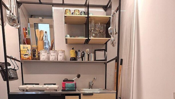 A compact kitchen with a sink, stove, and shelves above.