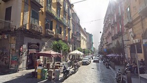 A cobblestone street lined with multi-story buildings, some with balconies and outdoor seating areas.