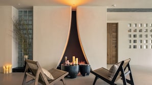 Een modern interieur met een centraal geplaatste open haard, twee houten stoelen en een decoratieve vaas.