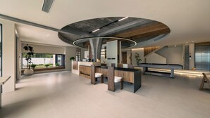 Een modern interieur met een pooltafel, zithoek en een groot raam met uitzicht op groen.