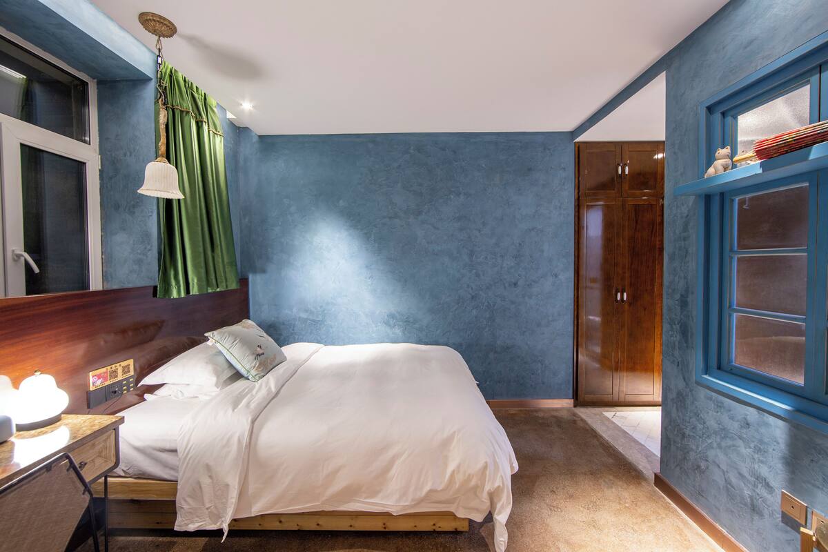 Un dormitorio con cama, mesita de noche, lámpara, armario y ventana con cortinas.