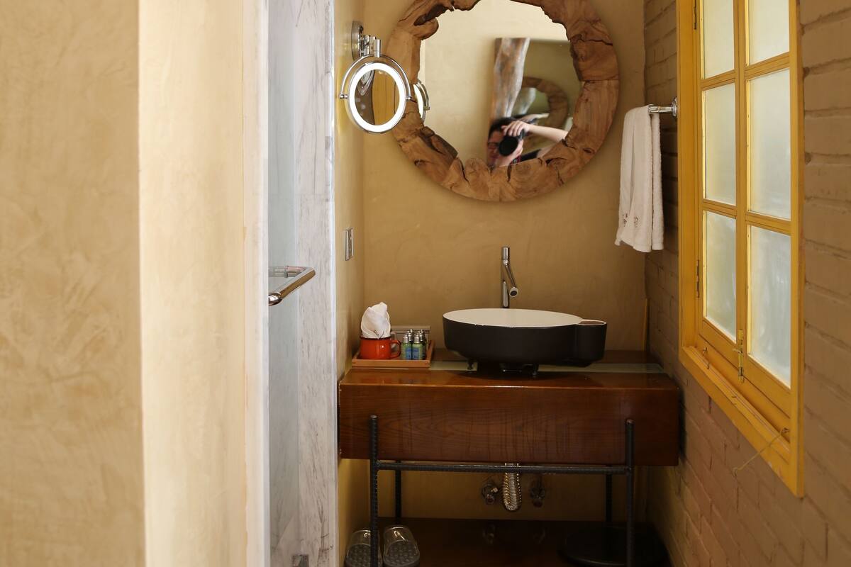 Un baño con un espejo redondo, tocador de madera y una ventana con vidrio esmerilado.