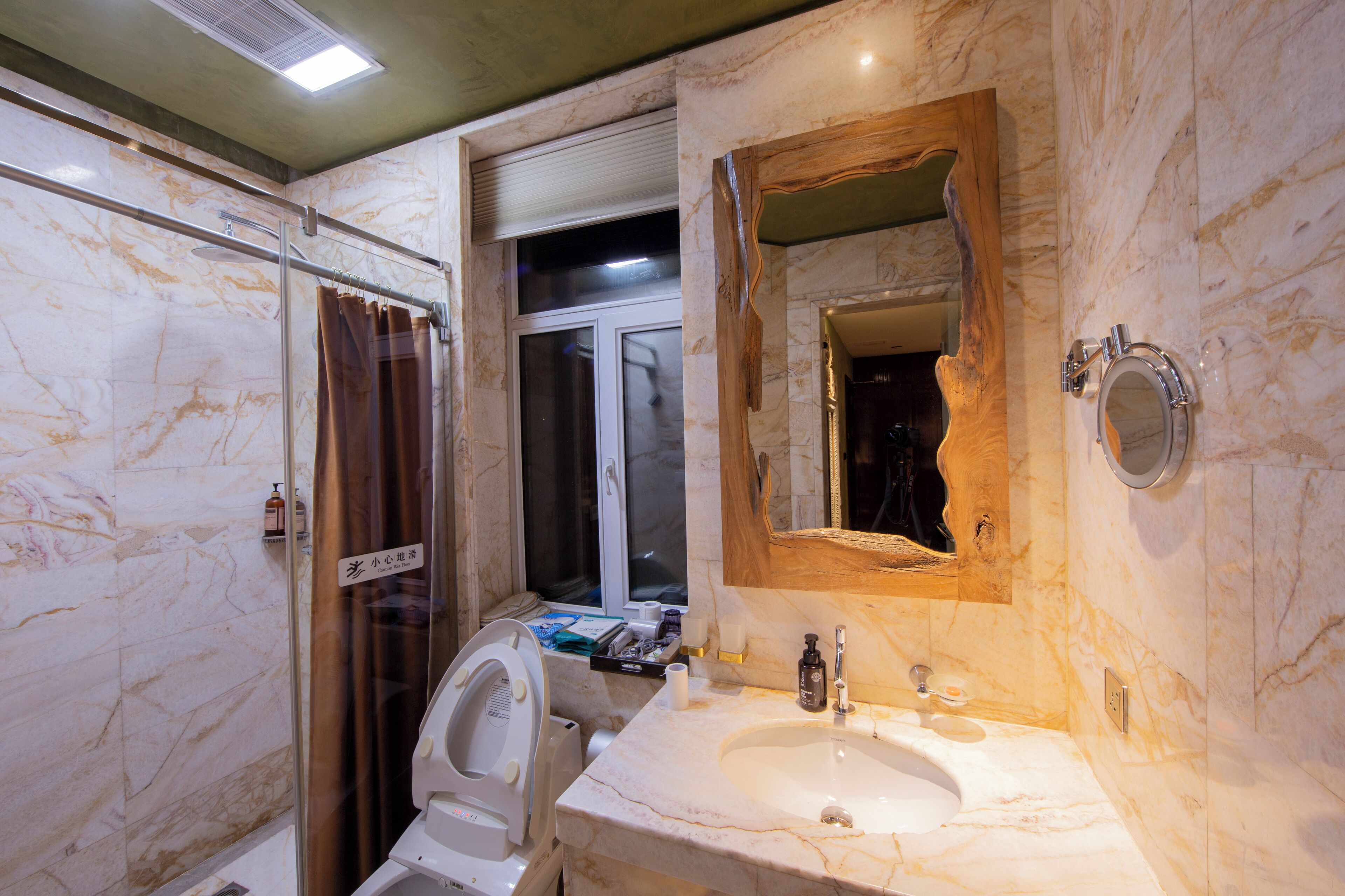 Un baño con lavamanos de mármol, cabina de ducha con paredes de vidrio y espejo con marco de madera.