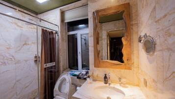 Un baño con lavamanos de mármol, cabina de ducha con paredes de vidrio y espejo con marco de madera.