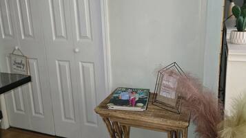 A wooden side table with a magazine, a decorative cross on the wall, and a cactus in a vase.