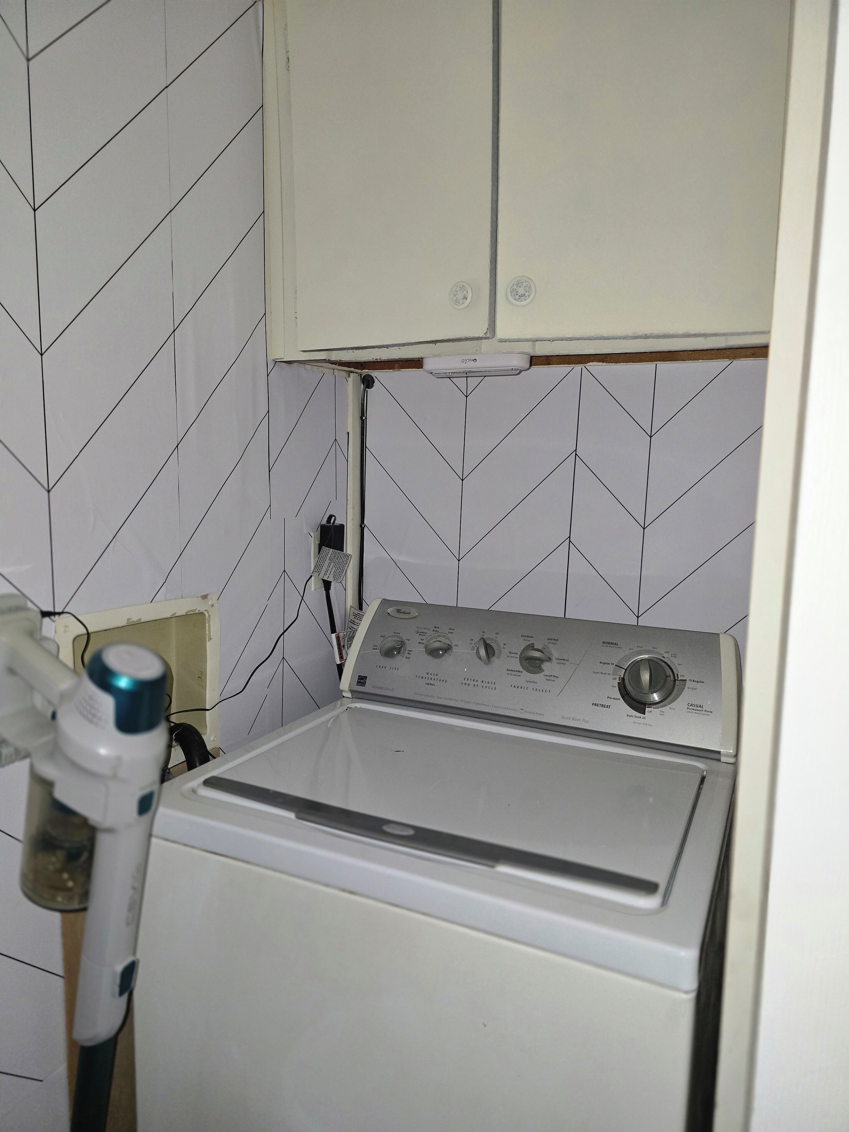 Una sala de bugaderia amb una rentadora i assecadora de càrrega frontal, un escalfador d'aigua i un rebedor de rajola blanca.