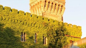 Un castillo con muros cubiertos de hiedra y un comedor con mesas y sillas blancas.