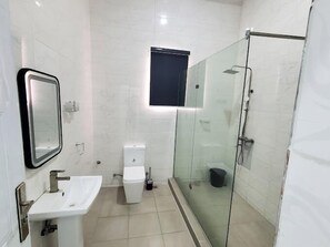 A modern bathroom with a glass shower enclosure, a white sink, and a toilet. - Fort Fountain Apartments (Abuja)
