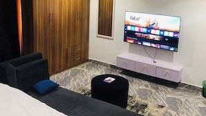 A modern hotel room with a large bed, a sofa, a TV mounted on the wall, and a wooden wardrobe. - Fort Fountain Apartments (Abuja)