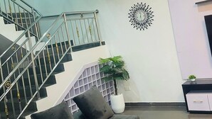 A modern living room with a staircase, a decorative wall piece, and a potted plant. - Fort Fountain Apartments (Abuja)