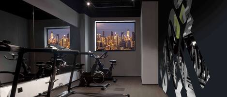 A gym with treadmills, stationary bikes, and a cityscape view through large windows.