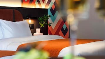 Hotellihuone, jossa on sänky, yöpöytä, lamppu ja seinä, jossa on geometrinen kuvio.