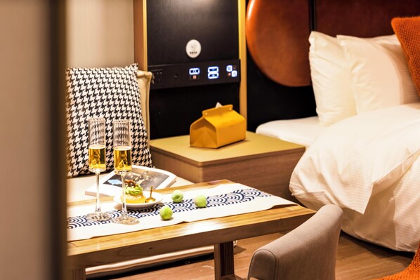 Une chambre d’hôtel bien aménagée, avec un lit, une table de chevet dotée d’une lampe, une petite table avec un set de table et un panneau de commande fixé au mur.