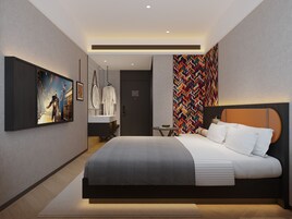 Una habitación de hotel moderna con una cama grande, televisión, baño con espejo y un diseño de pared colorido.
