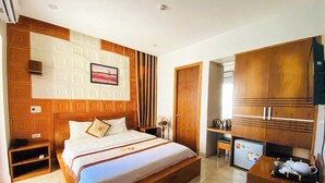 A hotel room with a large bed, wooden headboard, a small kitchenette, and a dining table.