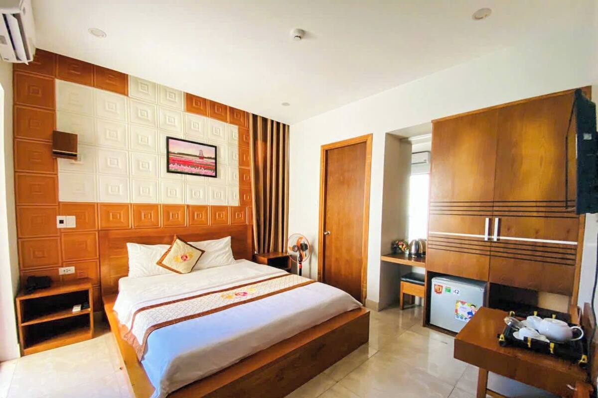 Habitación de hotel con una cama grande, cabecera de madera, una kitchenette pequeña y una mesa de comedor.