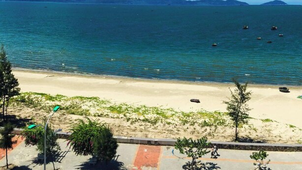 A beach with clear blue water, a sandy shore, and mountains in the background.