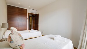 A hotel room with two beds, a wooden wardrobe, a bedside table with a lamp, and an air conditioning unit. - Comtat Muro 2 by Rentallorca (Muro)