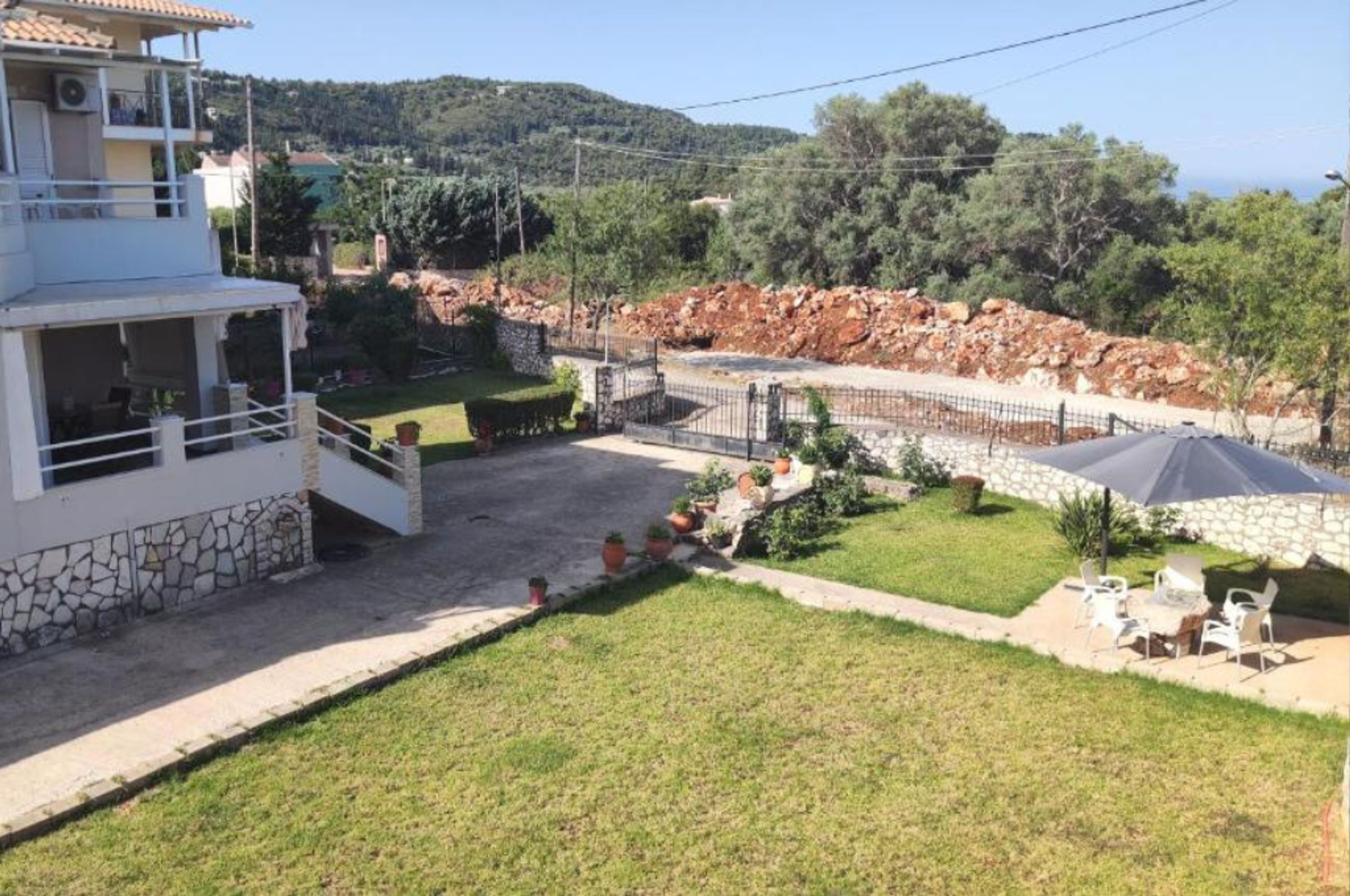 Zona residencial amb un edifici blanc, una paret de pedra i un carrer pavimentat.